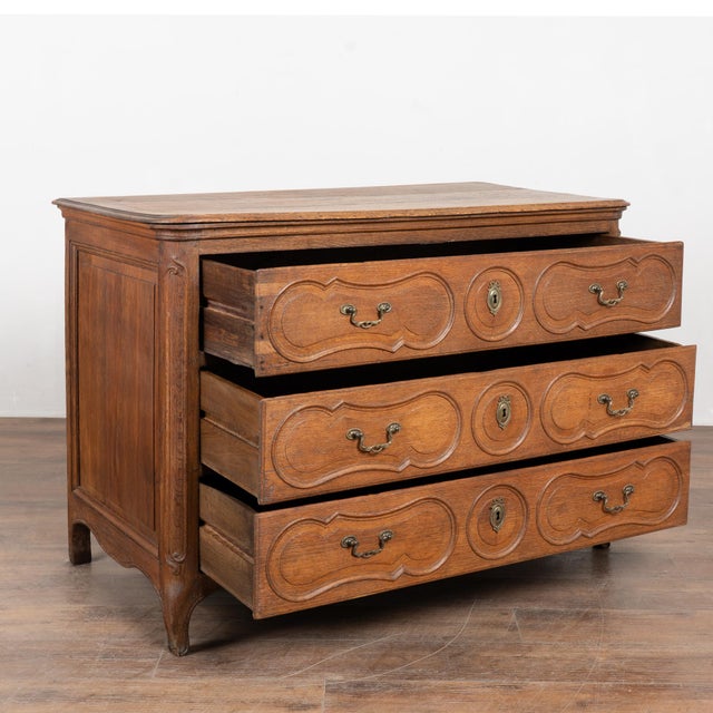 Late 18th-century French oak chest of three drawers featuring decorative paneled drawer fronts and curved canted sides...