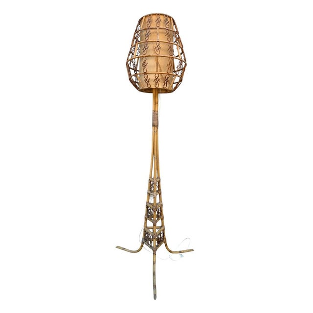 A French-inspired rattan floor lamp in the Louis Sognot style. The rattan tripod base and cage-shaped shade are...