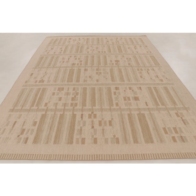 This handwoven wool 9x12 Art Deco rug features a geometric pattern of vertical bands and pixel-like motifs in soft ivory...
