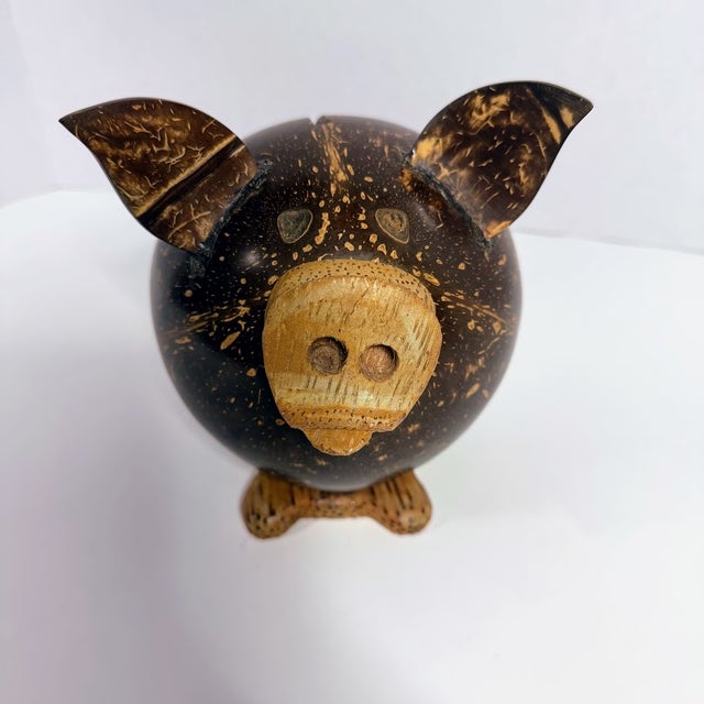 Handcrafted piggy bank carved from a real coconut shell, showcasing natural textures and a charming rustic aesthetic. This...