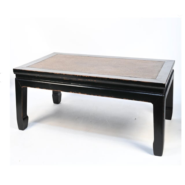 A Chinese black lacquered kang-style coffee tables with a rectangular top, woven rattan inset panel, mitered black lacquer...