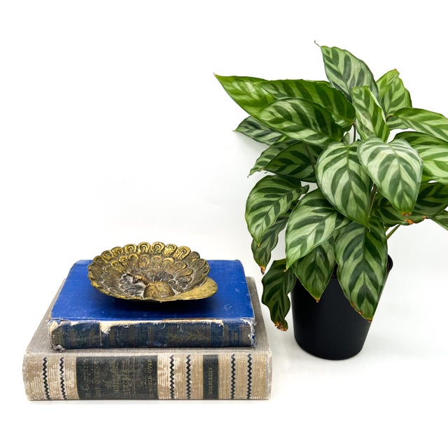 Striking vintage brass dish featuring a beautifully detailed peacock with its tail fully fanned in a dramatic circular...