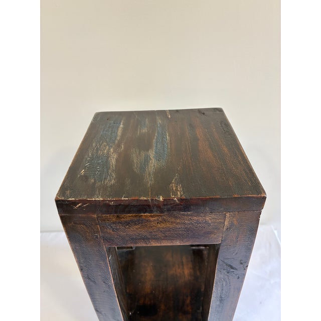 This solid pine stand features a two-tier open design with a square tabletop above a lower shelf, finished in a rich dark...