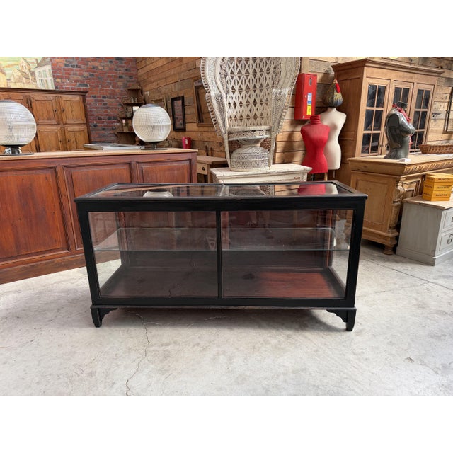This vintage glass-fronted display case has been fully restored. It features a black-patinated cabinet body; its three...