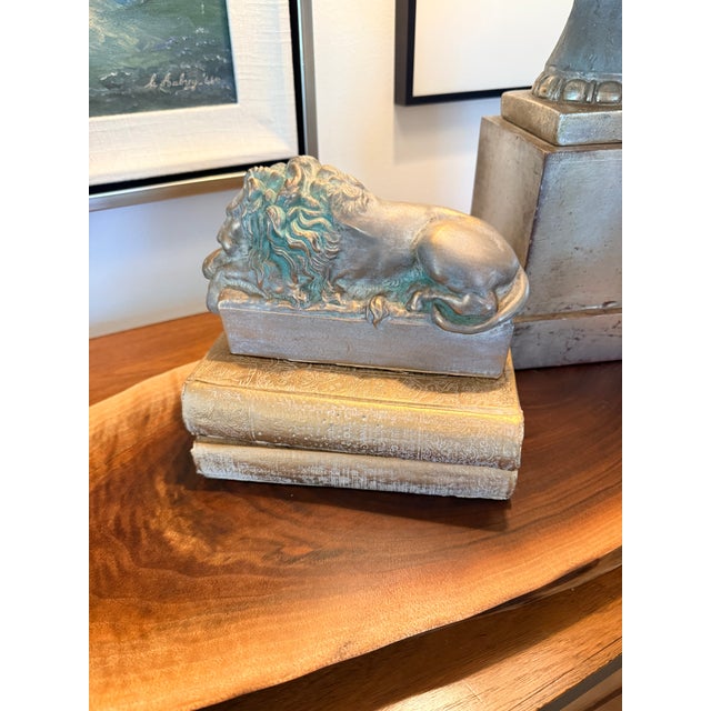 An exceptional sculptural lion resting atop a stack of decorative books, rendered in heavy cast metal and finished with a...