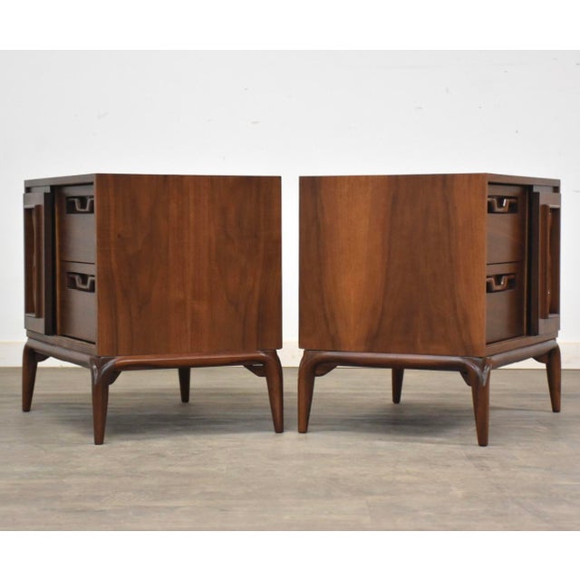 A pair of mid century modern walnut two drawer nightstands with sculpted pulls and a single sliding door. Circa 1960’s....