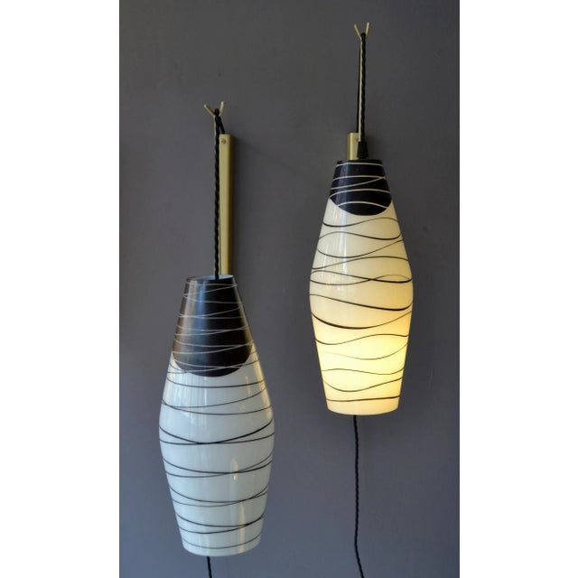 Pairs of wall-mounted pendants with opaline shades hand-painted in black hanging of black braided flex on an adjustable...