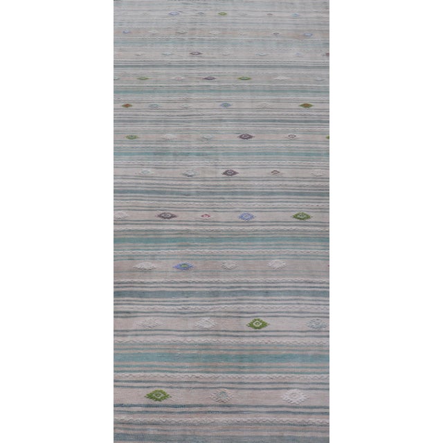 This flat-weave tribal Turkish kilim has been hand-woven in wool. The rug features an all-over sub-geometric striped...