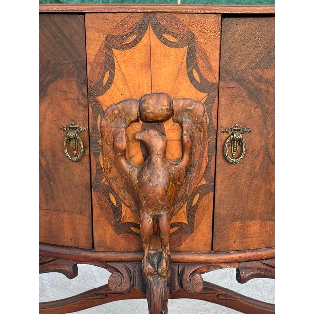 An unusual demilune low cabinet with bookmatched burl walnut doors flanking a marquetry center panel, mounted with a...