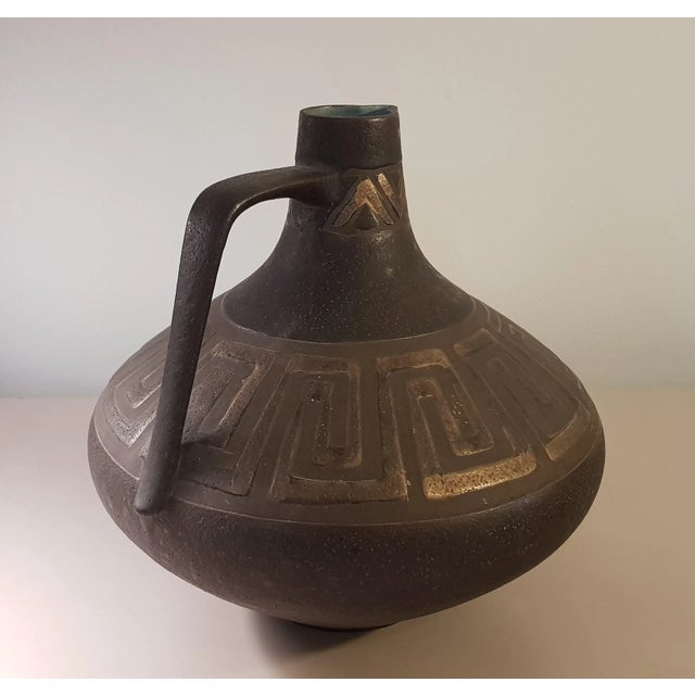 The matte brown glaze provides the ground for the bronze shimmering, meandering decor. From the neck of Henkelvase shines...