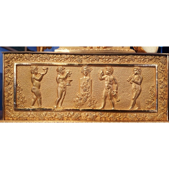 Chiseled and mercury-gilded bronze clock depicting a bacchanalian scene. The female figure holds a bunch of grapes with...