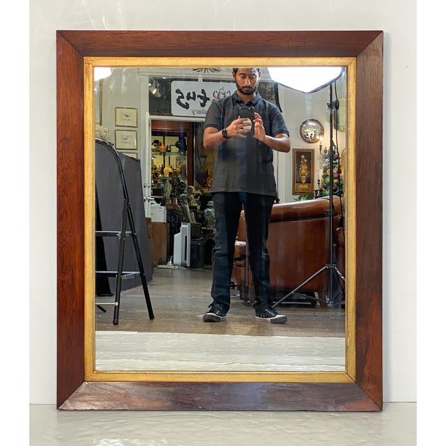 A fine large English rectangular mirror in the Empire style featuring a richly patinated mahogany frame with gilt inner...