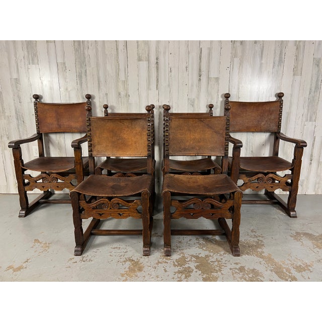 Set of six antique rustic Renaissance style solid oak hand carved dining chairs with thick saddle leather and large brass...