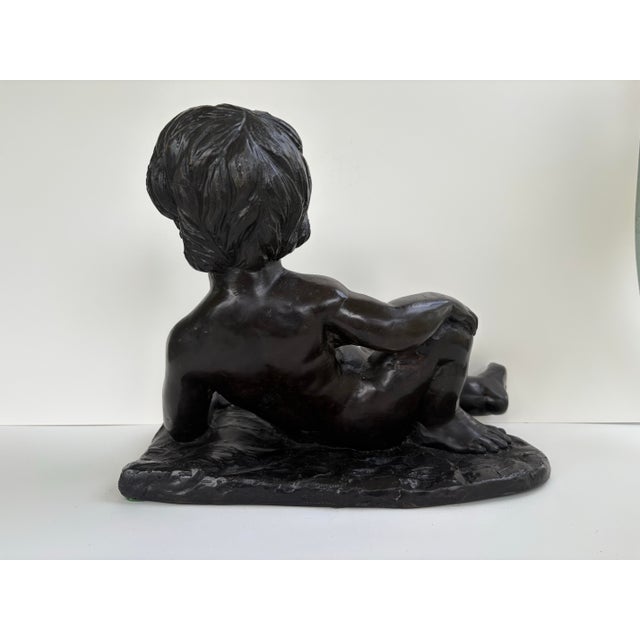 A beautifully sculpted vintage reclining cherub sculpture, rendered in a rich dark bronze finish with a soft, time-earned...