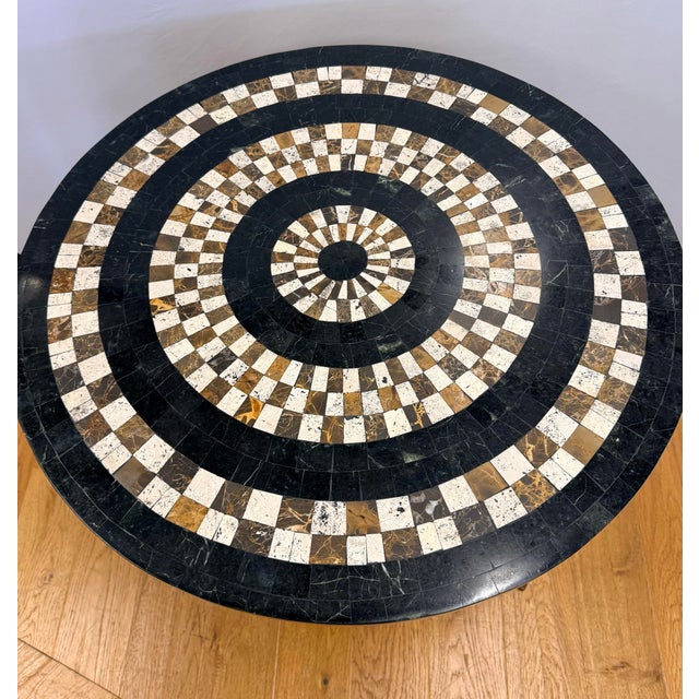 The dramatic marble top specimen table features an intricate geometric mosaic pattern—concentric circles of cream and dark...