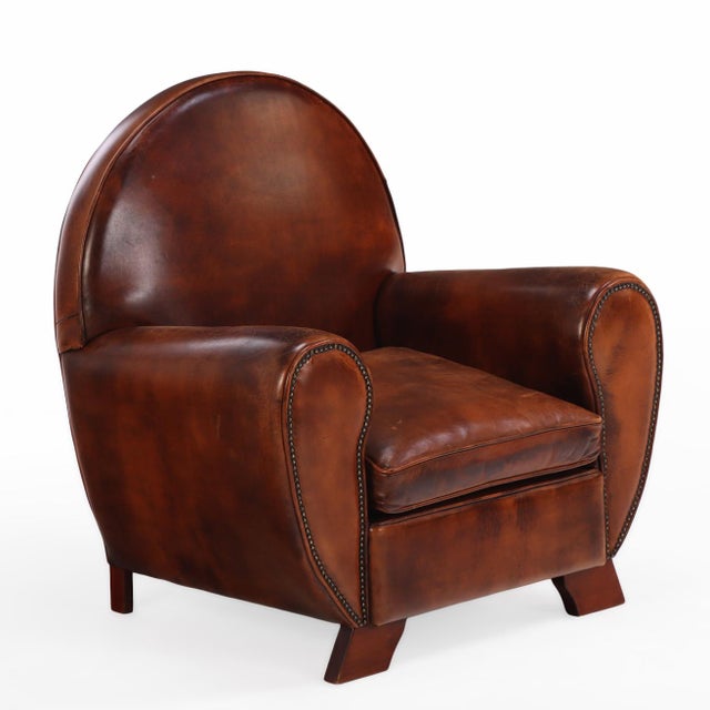 An early 20th-century Dutch leather club chair with matching ottoman in the Art Deco style. The chair features a rounded...