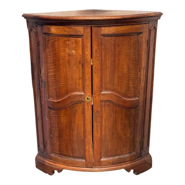 A French corner cabinet in walnut, the bowed front with a pair of shaped panel doors centered by a pierced brass...