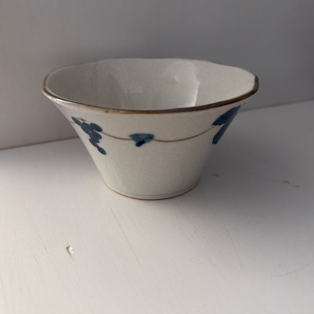 This off-white small ceramic bowl with crackle glaze features angled sides and is decorated with a charming French Blue...