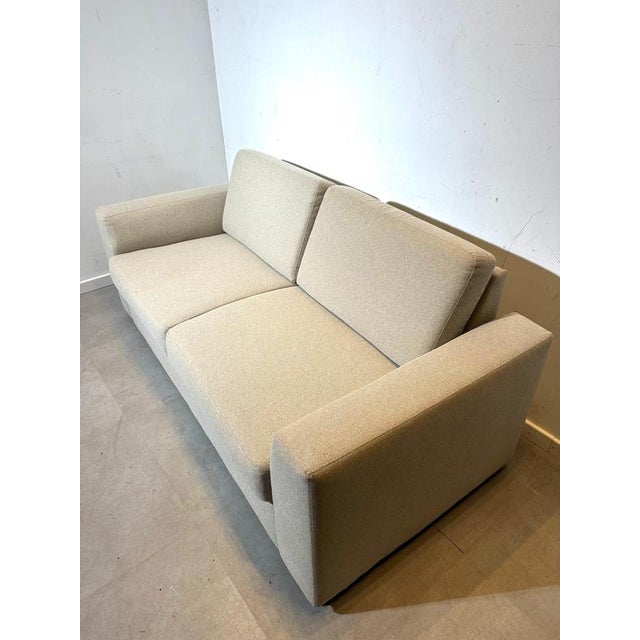 A clean and contemporary 3-seater sofa in a soft beige fabric, designed with wide geometric armrests and a low, modern...