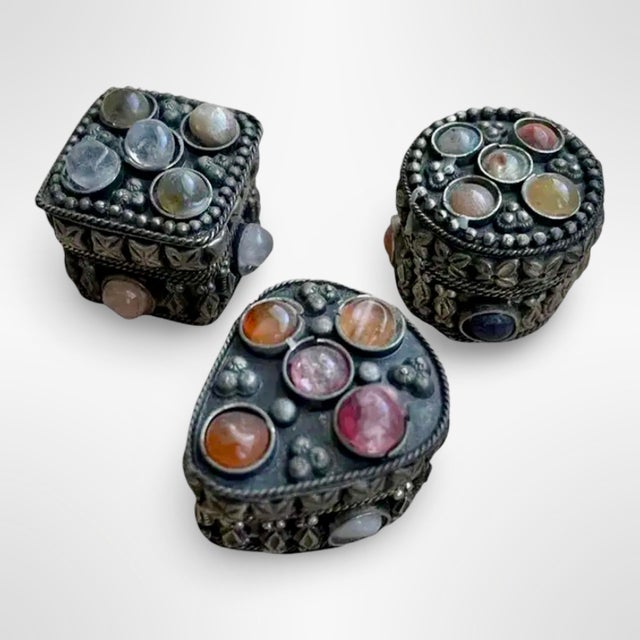 This set of three vintage mixed metal trinket boxes features ornate metalwork accented with embedded polished gemstones....