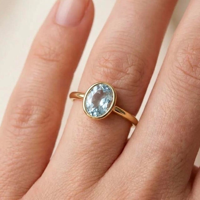 Oval Aquamarine Solitaire Ring in Gold Light, serene, and beautifully understated, this ring features a tranquil oval-cut...
