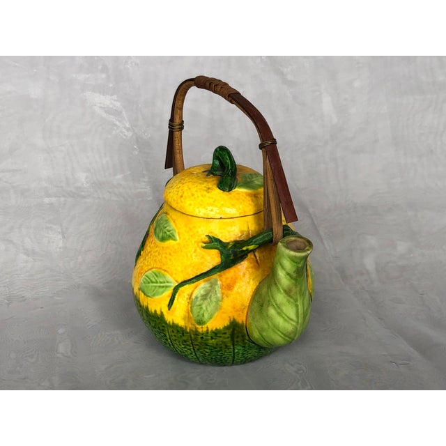 This charming decorative ceramic teapot made in the Majorlica style has a bamboo handle attached to branches on the pot's...
