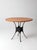 A vintage mid-century round dining table with a richly aged leather-covered top, sculptural iron base, and brass nailhead...