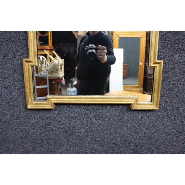 Elegant giltwood wall mirror featuring a tall arched form with stepped molding details and a softly sculpted crest at the...