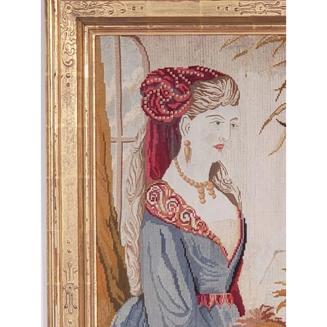 A framed needlepoint picture of a Victorian lady with parrot in a formal room, England circa 1880.