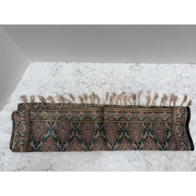 Vintage colorful silk fabric table runner in elegant gold, black and blue color woven patterns and gold knotted fringe on...