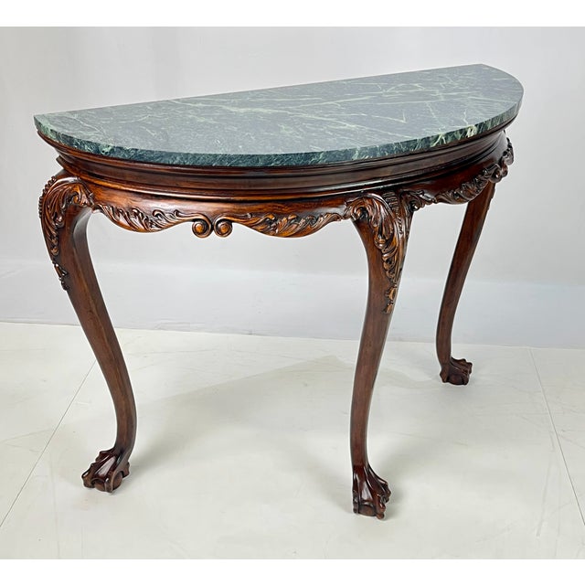Chippendale-style demilune console table featuring a richly veined, fitted dark green marble top. The carved wood frame...