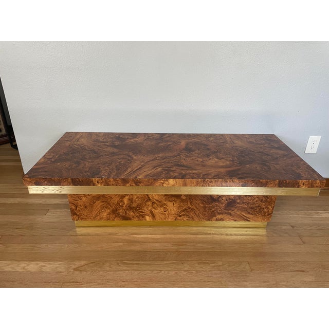 Elegant 1970s burlwood veneer coffee table with a dramatic architectural silhouette and polished brass banding. The...
