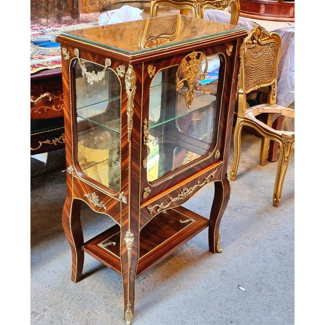 Elegant and refined, this petite French Louis XV-style display cabinet is crafted from richly finished wood and adorned...