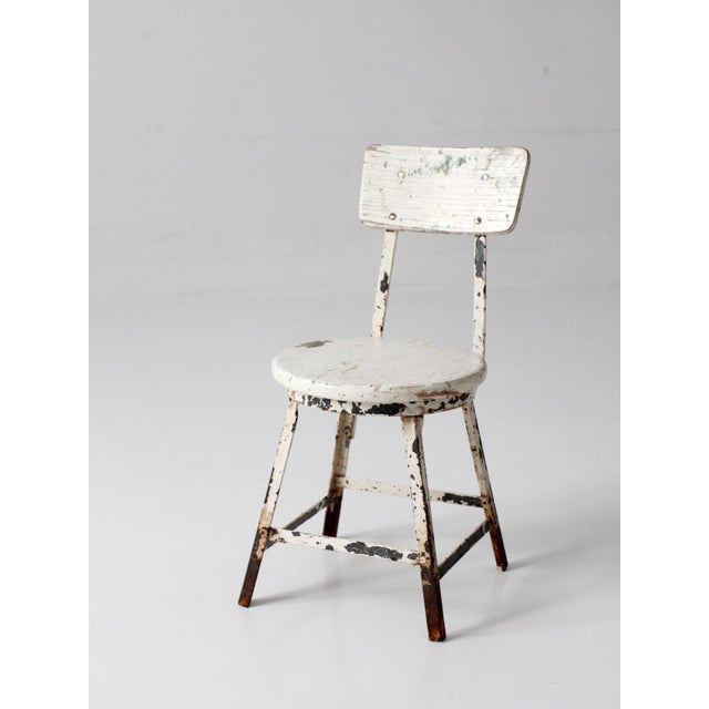 A vintage child’s chair, circa 1930s–1950s, with a painted wood seat and back set on a simple metal frame. The form draws...
