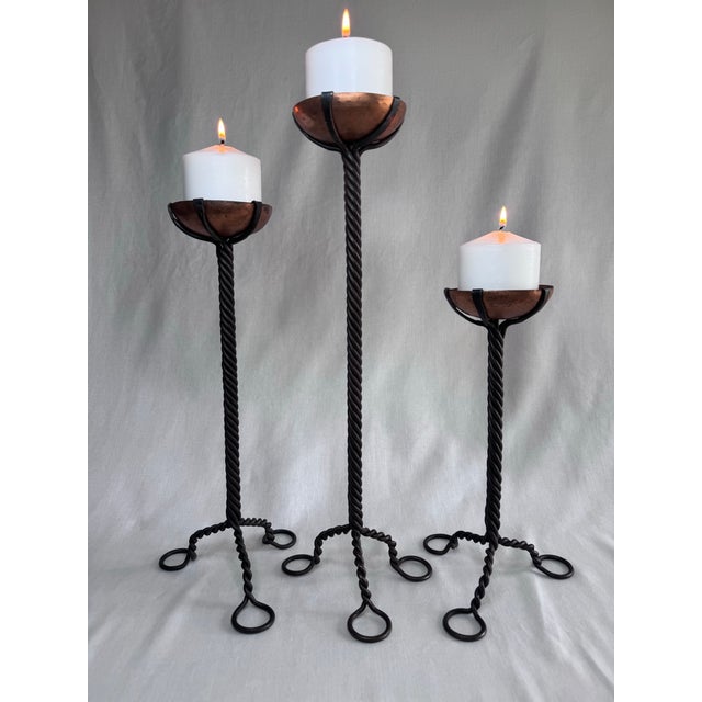 This is a striking set of three vintage Brutalist hand-forged metal candlesticks. Each holder has a warm copper...