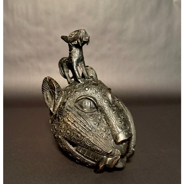 A cast bronze sculpture representing a stylized leopard head surmounted by a standing feline, attributed to Edo artists of...