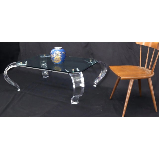 Mid-Century Modern glass top carved Lucite cabriole leg rectangular coffee table. The legs are secured and brass ball...