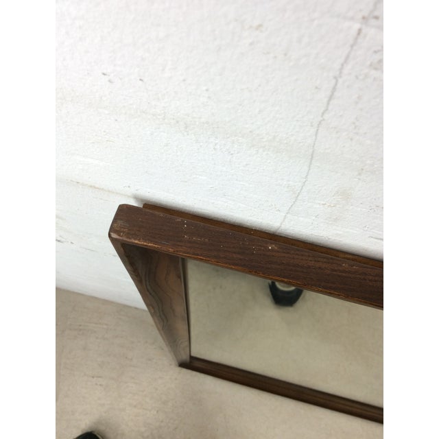 This mid century modern mirror features long rectangular hardwood frame, original walnut finish, and vintage mirrored glass.