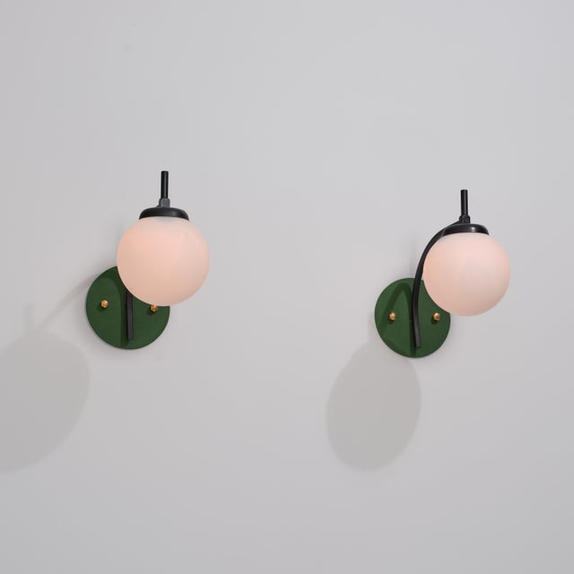 Pair of italian wall sconces from the 1950s, defined by a curved black lacquered brass stem, spherical opaline glass...