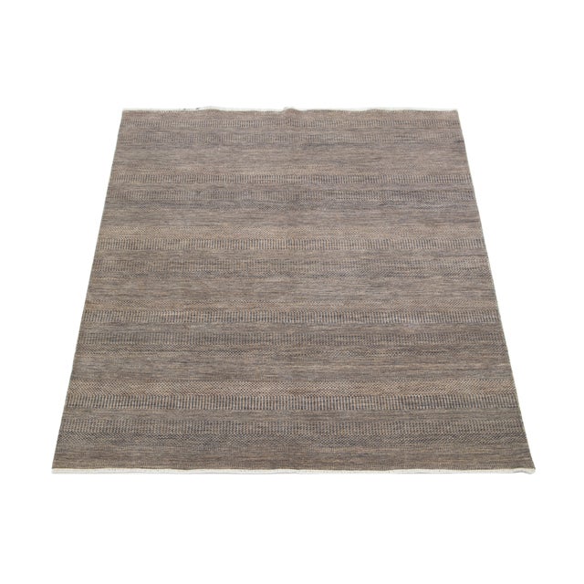 This elegant hand-knotted wool rug features a contemporary design. It showcases a meticulously crafted field in brown...