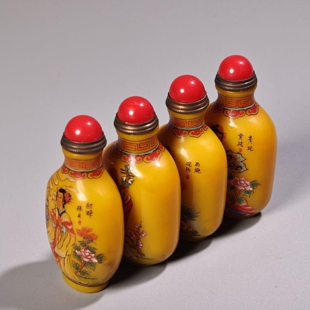 This is a set of four matching yellow glass snuff bottles, each featuring a hand-painted portrait of one of the "Four...
