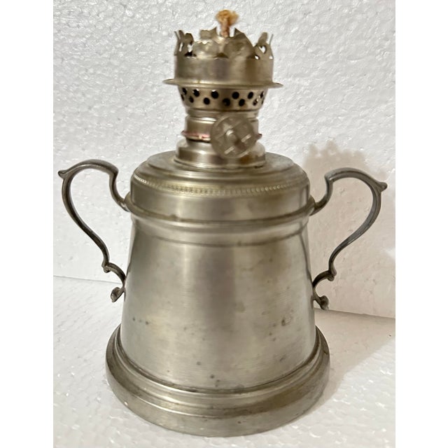 This vintage pewter lamp features a classic oil lantern design with a central wick burner, a fount for holding fuel, and...