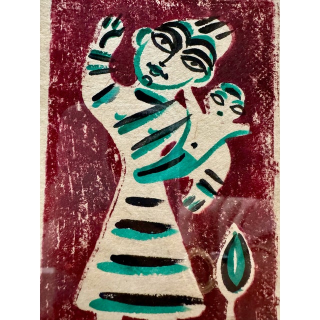 Small vintage folk art painting on textured paper depicting a stylized mother carrying a child, rendered in burgundy,...