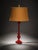 A vintage-style red glass table lamp with a glossy decorative base and a warm burlap-style fabric shade. The bold red base...