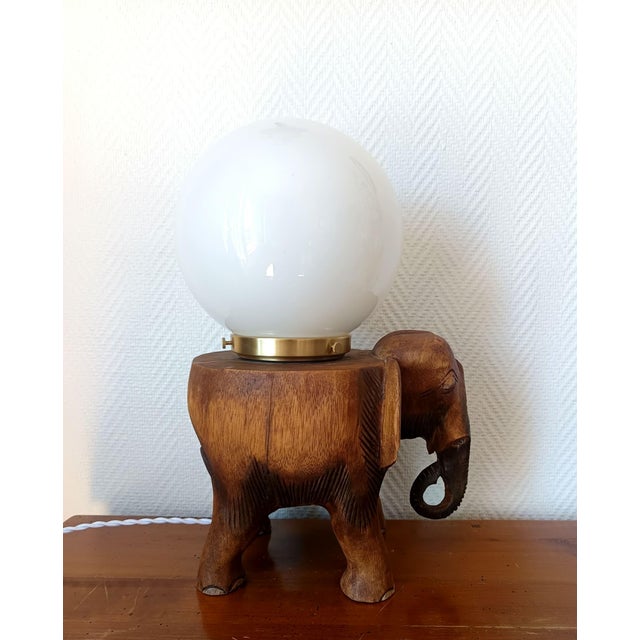 Stunning solid wood sculpture of an elephant, mounted as a table lamp/nightlight with a white opaline glass shade. Gold-...