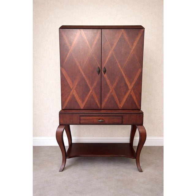 Art deco style bar cabinet in a dark wood finish with a distinctive geometric inlay pattern. The interior is lighted and...