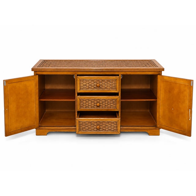 A distinctive vintage credenza featuring a warm honey-brown wood finish with woven rattan or cane-style detailing. The...