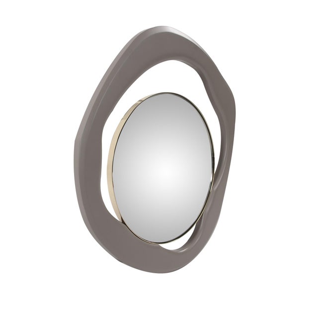 A traditional polished gold round stainless steel framed mirror appears to be balancing in the abstract. The gray matte...