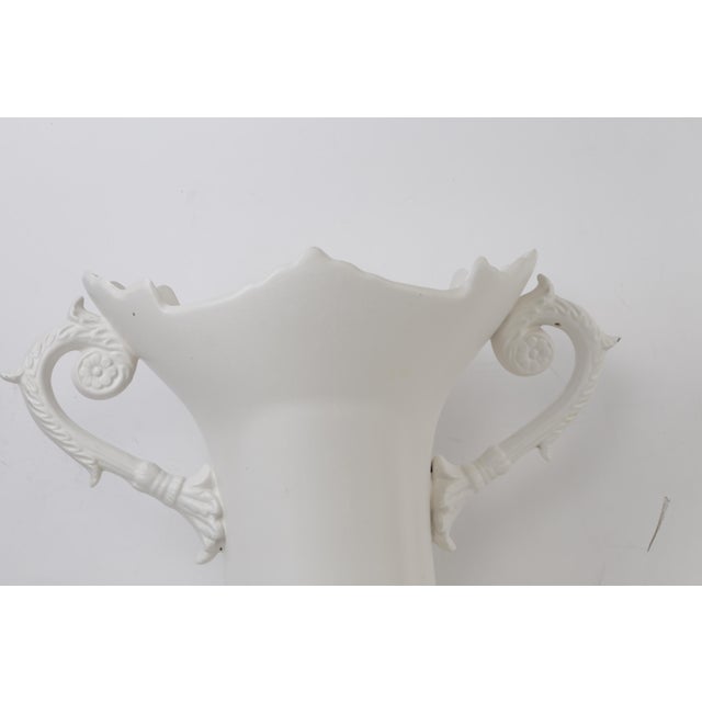 Elegant white porcelain urn vase featuring a beautifully sculpted silhouette with ornate scroll handles, a scalloped rim,...