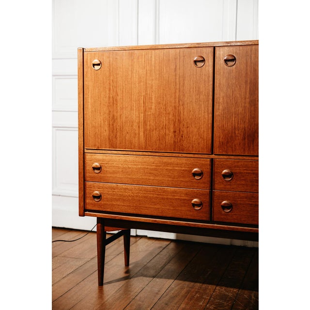 This 1960s teak bar cabinet embodies the tradition of post-war Scandinavian design. Its tapered legs, recessed circular...